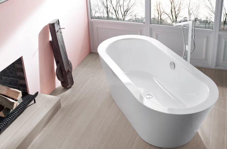 Bañera ovalada exenta de acero esmaltado en baño moderno con gran ventana y baldosas imitación madera.